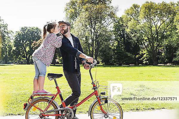 Daughter kissing father with bicycle in a park