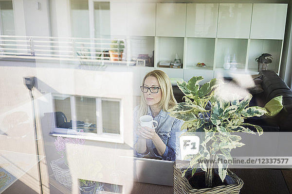 Mature businesswoman sitting at table with cup of coffee looking out of window