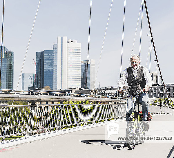 Smiling mature man on bicycle crossing bridge in the city
