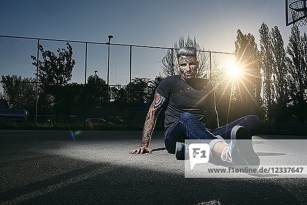Portrait of tattooed young man sitting on basketball court at sunset