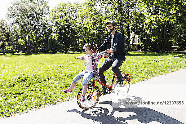 Happy father riding bicycle with daughter in a park