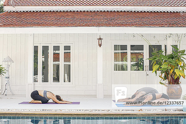 Two women and a man practicing yoga at the poolside