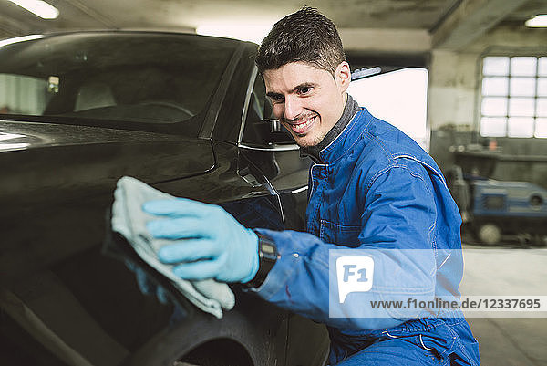 Smiling man cleaning a car in a workshop