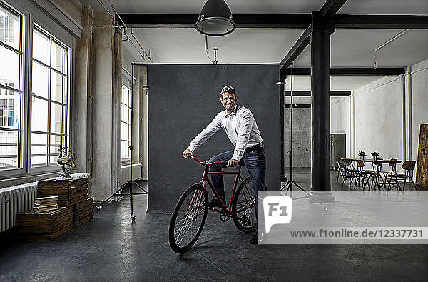 Portrait of mature businessman on fixie bike in front of black backdrop in loft