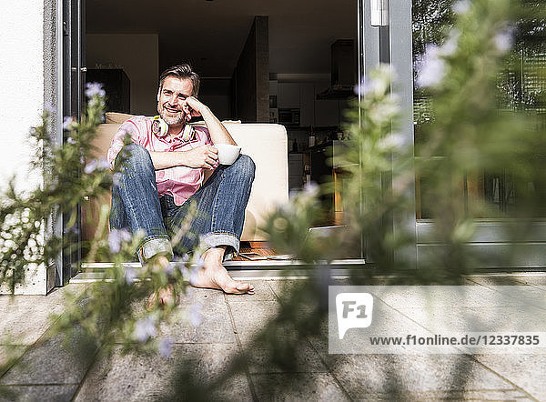 Content man sitting with cup of coffee at open terrace door