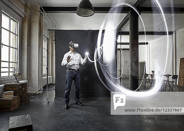 Mature man with vr glasses light painting in front of black backdrop in loft