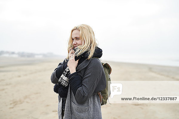 Portrait of blond young woman with backpack on the beach in winter