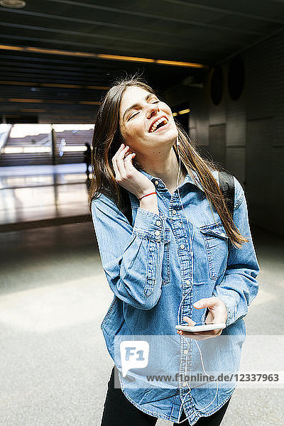Portrait of happy young woman listening music with cell phone and earphones
