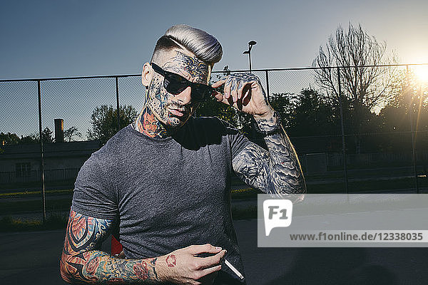 Portrait of tattooed young man wearing sunglasses smoking a cigarette