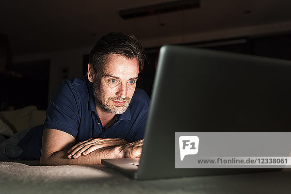 Portrait of man lying on couch at home looking at laptop