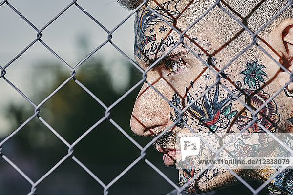 Tattooed face of young man behind fence
