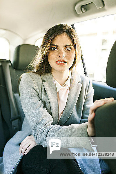 Portrait of young businesswoman sitting on backseat of a car