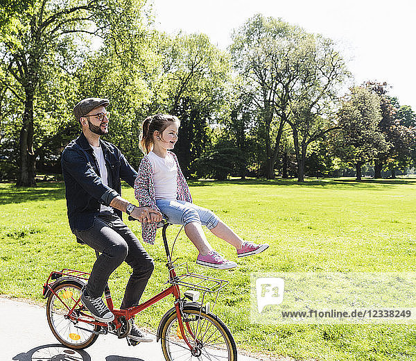 Happy father riding bicycle with daughter sitting on handlebar in a park