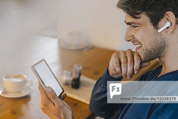 Smiling man in a cafe with earphone using tablet