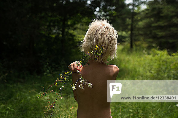 Blondhaariger Junge im Wald mit einer Wildblume auf der Schulter  Rückansicht