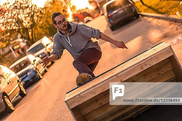 Junger männlicher Skateboarder dreht sich bei Sonnenuntergang auf der Vorstadtstraße und fährt die Rampe hoch