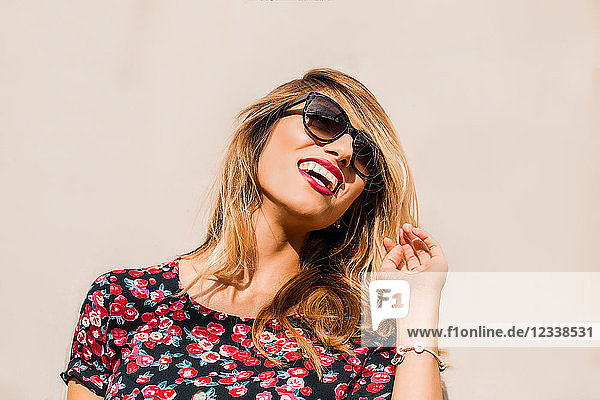 Blond  stylish mid adult woman wearing sunglasses in front of wall laughing