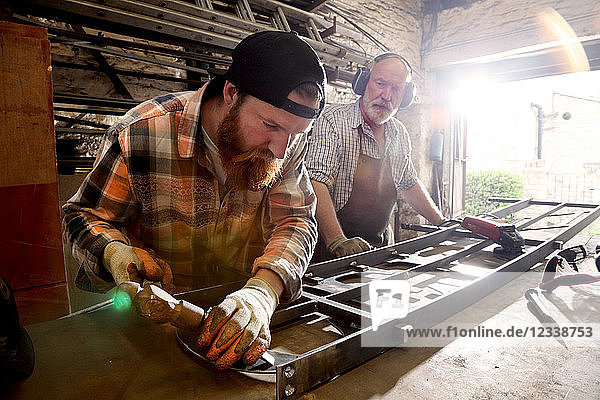 Senior blacksmith and son hammering metal on workbench in blacksmiths shop