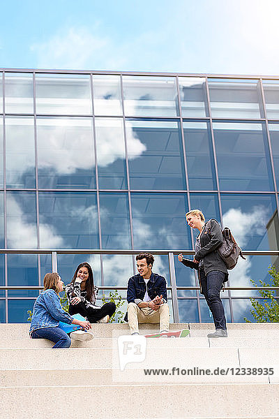 Vier junge erwachsene Studenten sitzen vor dem College auf einer Treppe und unterhalten sich