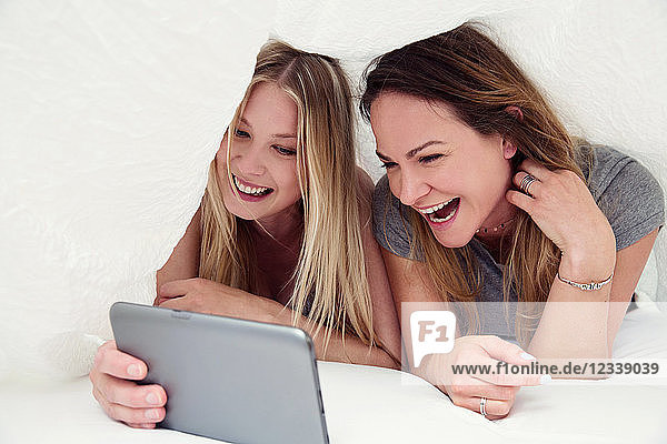 Freunde unter dem Bettlaken mit digitalem Tablet lächeln