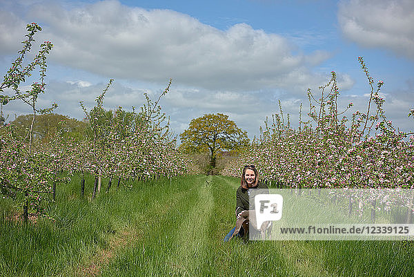 Woman kneeling with her dog in blossoming orchard  portrait