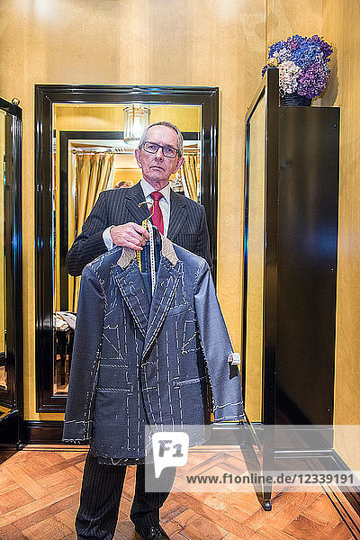 Tailor holding unfinished bespoke jacket in tailors shop  portrait
