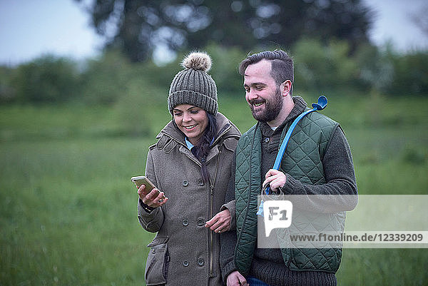 Man and woman walking arm in arm across field looking at smartphone