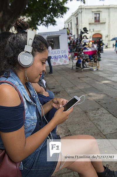 A young woman is texting and listening to music on the square in front of the Cathedral of Our Lady of the Assumption in the city of Oaxaca de Juarez  Oaxaca  Mexico.