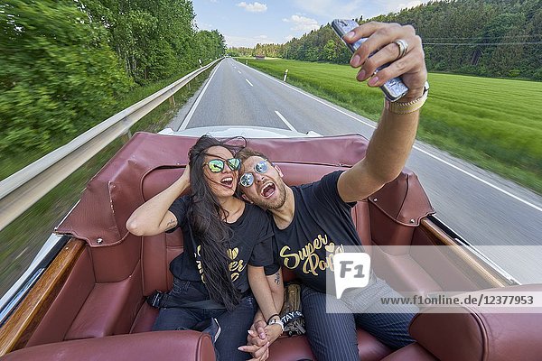 Adventurous couple taking selfie while driving in luxury oldtimer. Turkish ethnicity. High society. Bloggers Adem Bayalan and Emine Feruz Bayalan. Bavaria Germany.