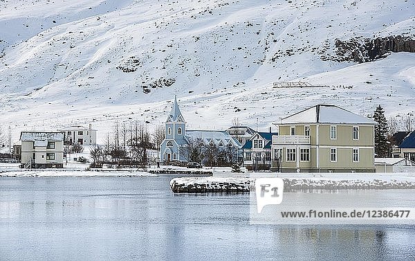 Blick auf die blaue Kirche Seyðisfjarðarkirkja im Dorf Seyðisfjörður mit Schnee  Spiegelung im See Fjarðará  Austurland  Ostisland  Island  Europa