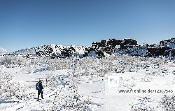 Mann auf Wanderweg im Schnee bei Sonnenschein  verschneite Landschaft  Lavafeld mit schneebedecktem Felsbogen  Vulkanlandschaft Krafla  Dimmuborgir Nationalpark  Mývatn  Island  Europa