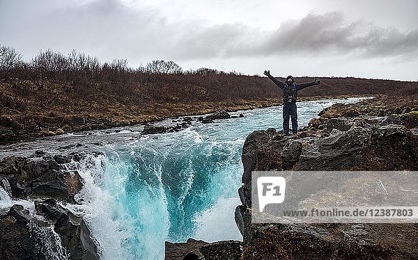 Tourist  junger Mann steht an einem Wasserfall am blauen Fluss Brúará  Südisland  Island  Europa