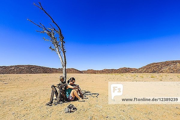 Junge Frau sitzt unter einem vertrockneten Baum neben einem Steinhaufen Einsamer Mann  Hartmanntal  Kunene-Region  Namibia  Afrika