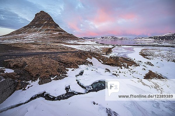 Kirkjufell mountain Kirkjufellfoss waterfall frozen up in front cloudy sky with sunset Grundarfjördur fjord western Iceland Iceland Europe