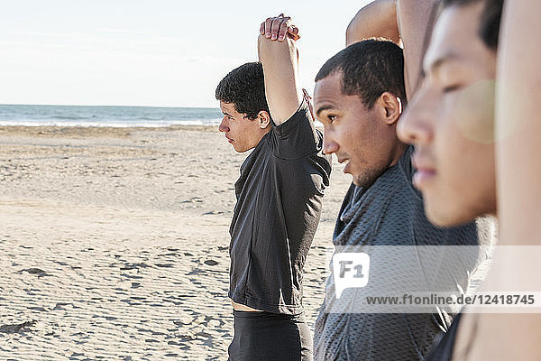 Male runners stretching arms on sunny beach