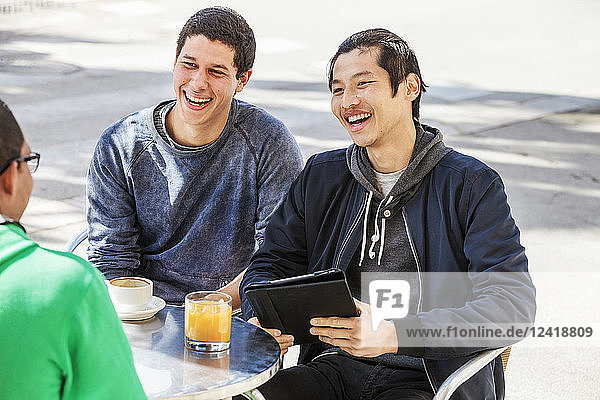 Male friends with digital tablet laughing at sidewalk cafe