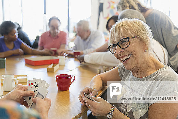 Happy senior woman playing cards with friend at table in community center