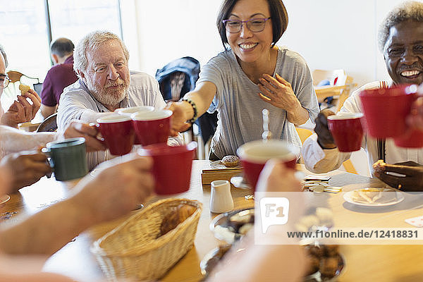 Happy senior friends enjoying afternoon tea  toasting mugs in community center