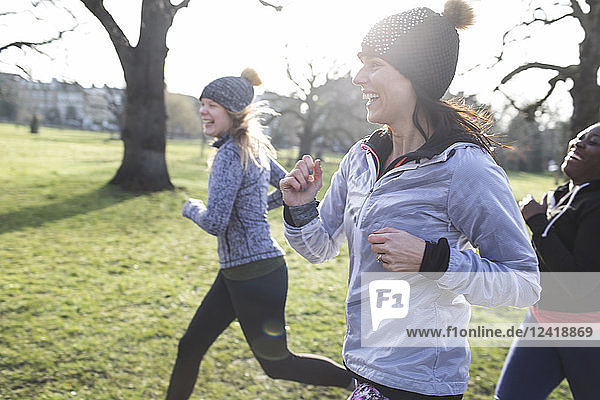 Smiling female runners running in sunny park