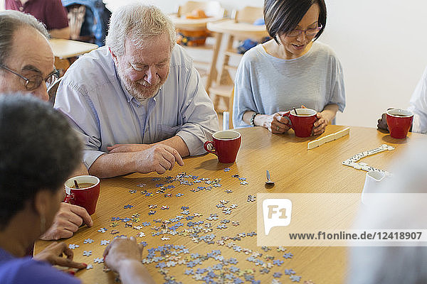 Senior friends assembling jigsaw puzzle and drinking tea at table in community center