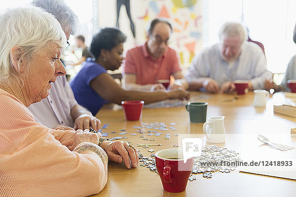 Senior woman assembling jigsaw puzzle with friends at table in community center