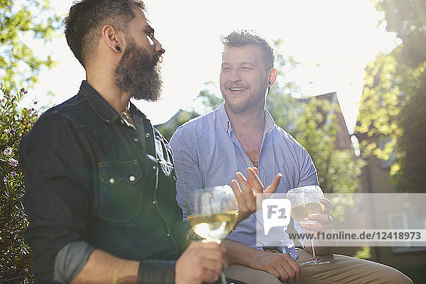 Smiling male gay couple drinking white wine in sunny garden