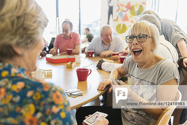 Happy senior woman playing cards with friend in community center