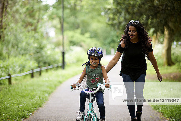 Happy mother teaching daughter how to ride bike