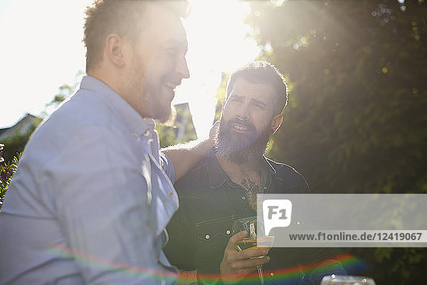 Affectionate male gay couple drinking wine in sunny garden