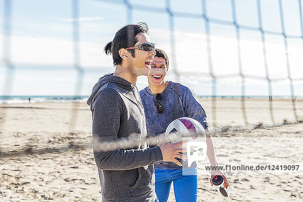 Happy male friends playing beach volleyball on sunny beach