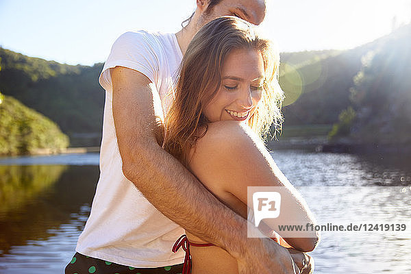 Affectionate couple hugging at sunny summer lake