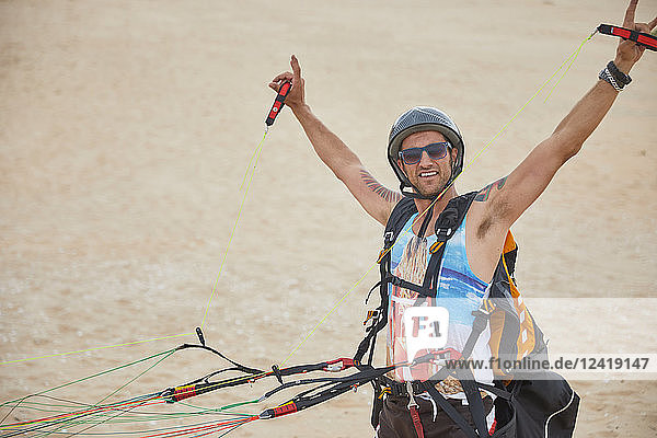 Portrait confident  carefree male paraglider strapped with equipment on beach