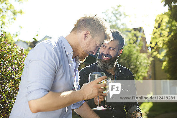 Happy male gay couple drinking wine in sunny garden