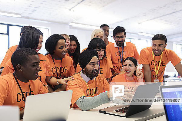 Happy hackers at laptop coding for charity at hackathon